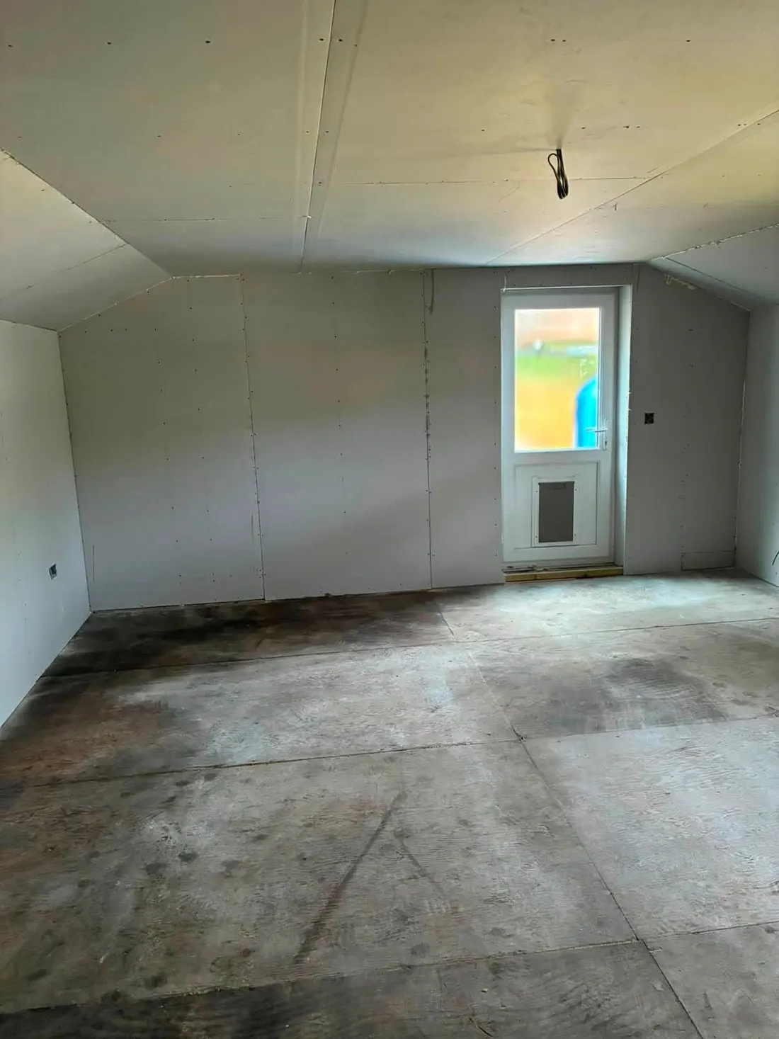 A plasterboarded room inside a barn conversion, ready for decoration, with an external door fitted