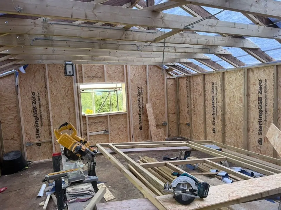 Timber roof trusses and OSB wall sheathing during a barn conversion, with power tools set up on a workbench