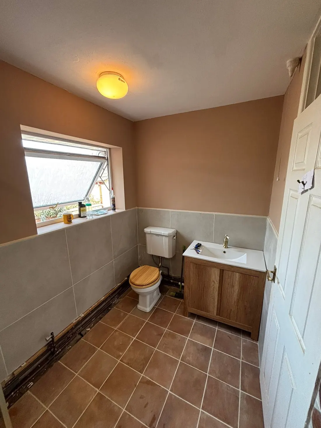 A finished bathroom with a tiled lower wall, fitted vanity unit and basin, toilet and tiled floor