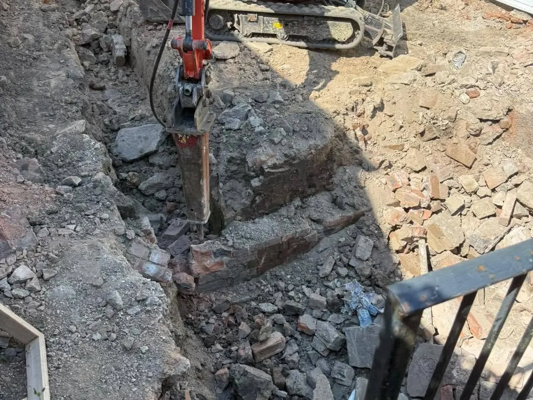 A hydraulic breaker attachment on a mini digger breaking up old brick and stone