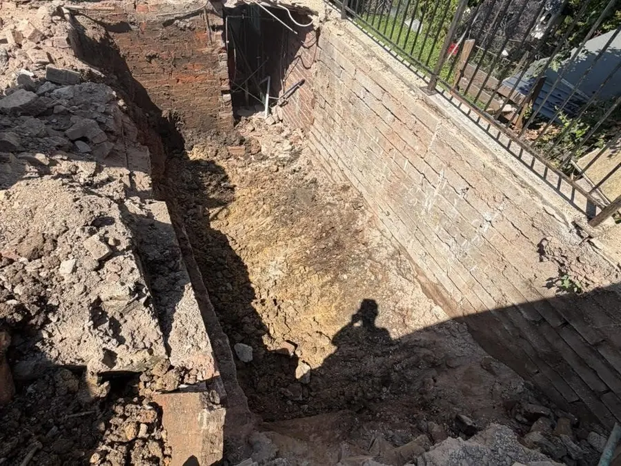 A deep trench excavated alongside a stone retaining wall, with the spoil cleared back