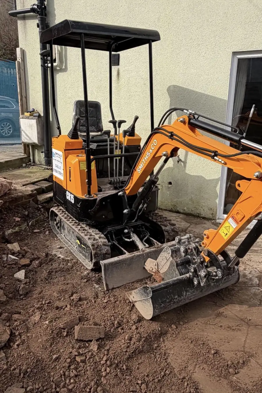 A Smiths & Co branded mini digger parked on a job, with the company name and phone number on the machine