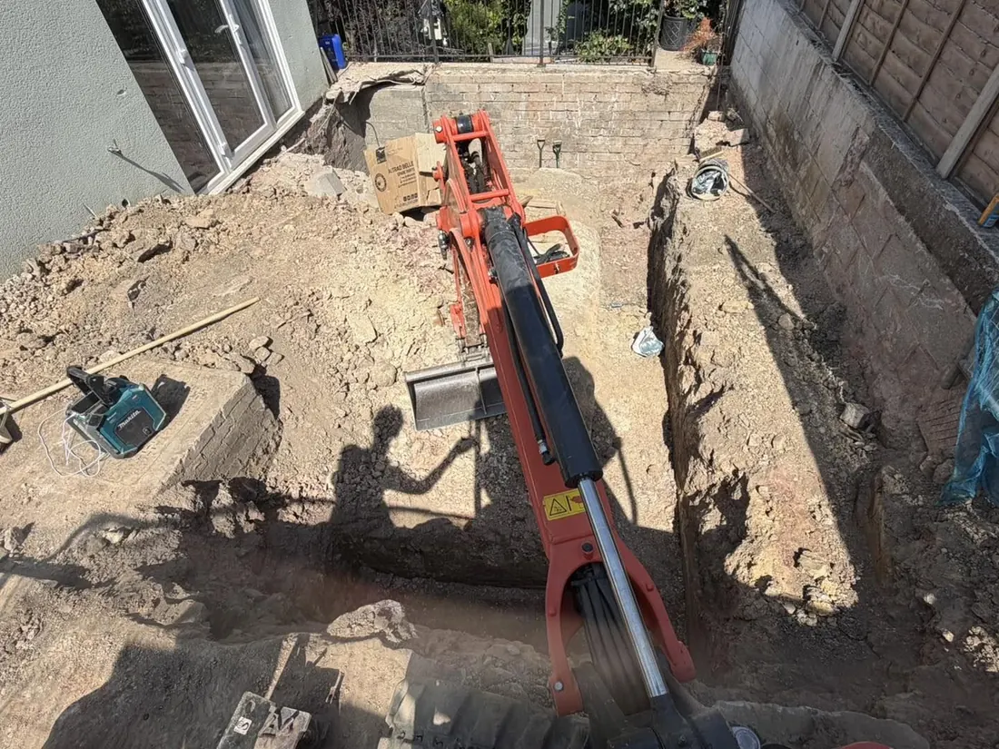 An operator&rsquo;s-eye view down into a freshly dug foundation trench running along the back of a house