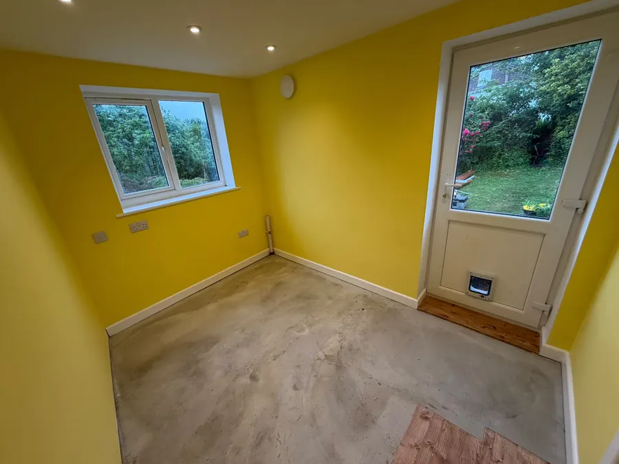 A room decorated in yellow with new windows and an external door, floor not yet laid
