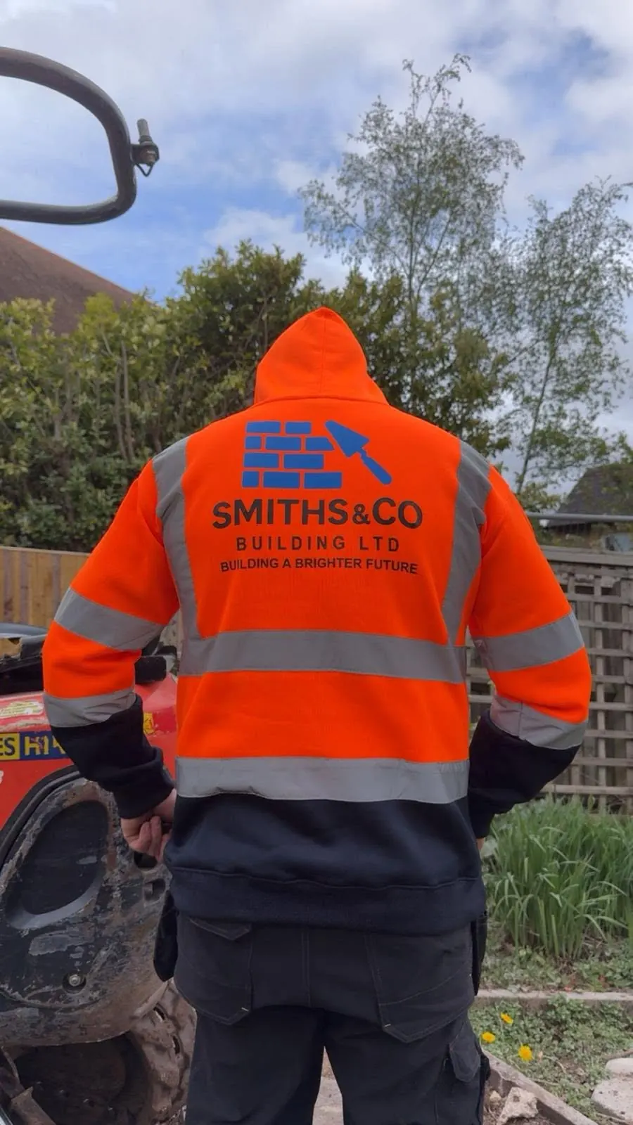 A Smiths & Co team member in branded hi-vis standing beside a mini digger on site