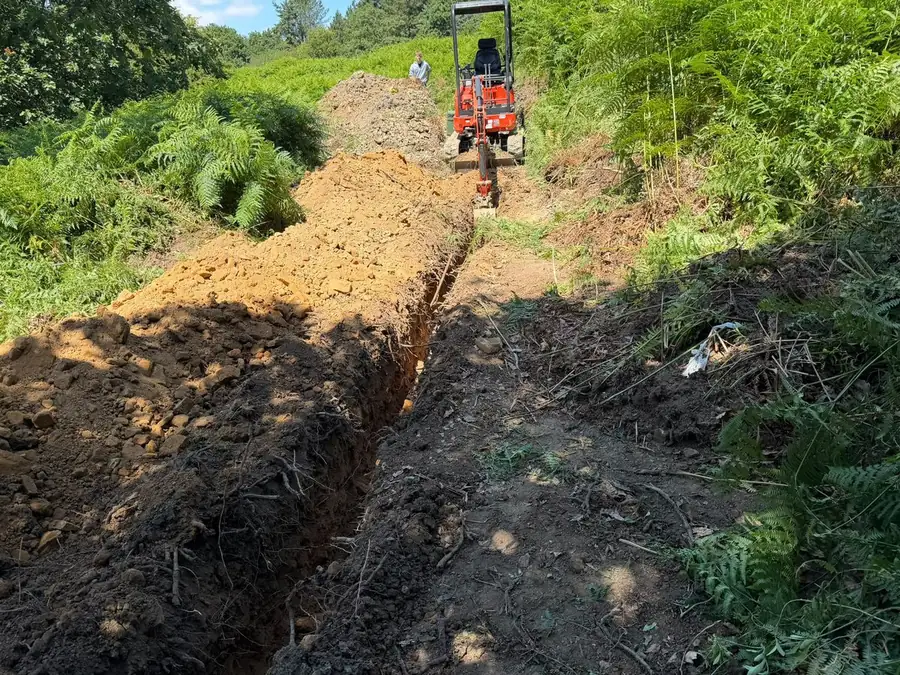 A trench cut across a steep bank with a mini digger at the top