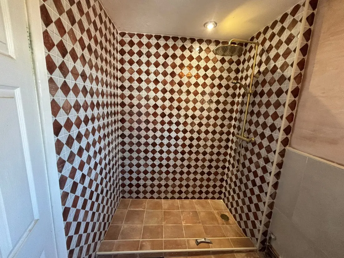 A fully tiled wet room with a rainfall shower and the floor laid to fall towards a central drain