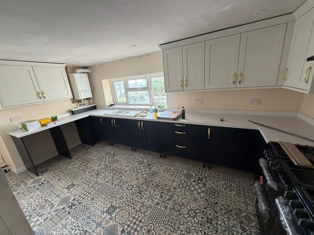The same kitchen from the far end, with cream shaker wall units, navy base units, brass handles and a patterned tile floor